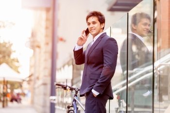Successful businessman with bicycle. Successful businessman in suit with bicycle in city talking over mobile phone