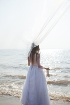 Bride is standing on the beach and holding her shoes