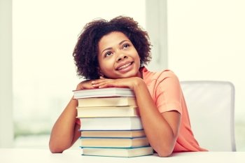 education, school, knowledge and people concept - happy smiling african american student girl with books sitting at table and dreaming at home