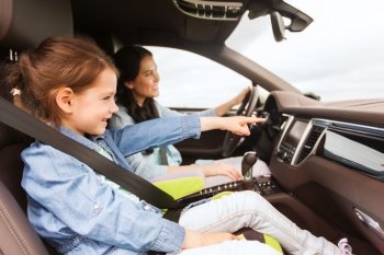 family, transport, road trip and people concept - happy woman with little daughter driving in car