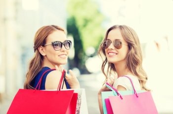 sale, consumerism and people concept - happy young women in sunglasses with shopping bags on city street
