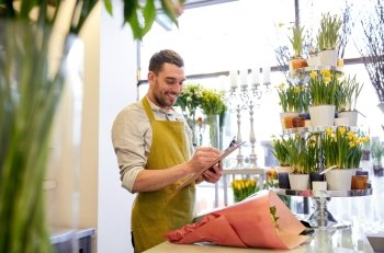 people, sale, retail, business and floristry concept - happy smiling florist man with bunch writing and making notes to clipboard at flower shop counter