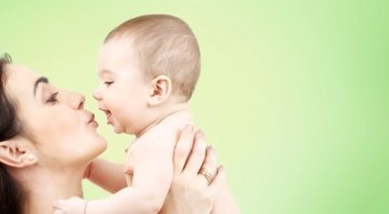 family, motherhood, parenting, people and child care concept - happy mother kissing adorable baby over green background