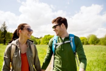 travel, hiking, backpacking, tourism and people concept - happy couple with backpacks holding hands and walking along country road outdoors