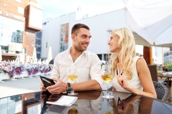 date, people, payment and finances concept - happy couple with wallet and wine glasses paying bill at restaurant