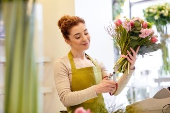 people, business, sale and floristry concept - happy smiling florist woman making bunch and cropping stems by scissors at flower shop
