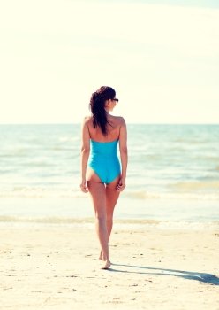 summer vacation, tourism, travel, holidays and people concept -young woman in swimsuit walking on beach from back
