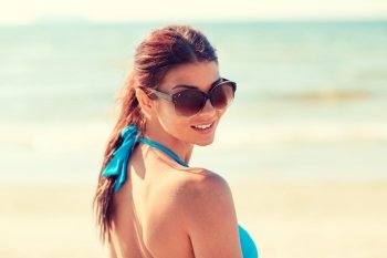 summer vacation, tourism, travel, holidays and people concept -face of smiling young woman in swimsuit with sunglasses on beach
