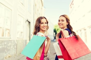 sale, consumerism and people concept - happy young women with shopping bags walking along city street and looking back