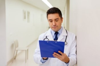 medicine, healthcare and people concept - doctor writing to clipboard at hospital