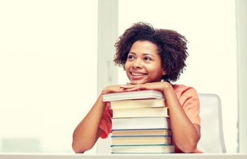 education, school, knowledge and people concept - happy smiling african american student girl with books sitting at table and dreaming at home