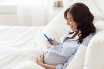 pregnancy, motherhood, technology, people and expectation concept - happy pregnant woman with smartphone in bed at home
