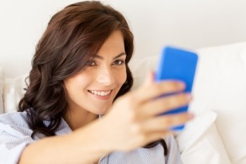 people, technology, communication and leisure concept - happy young woman with smartphone taking selfie at home