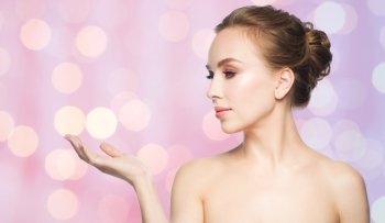 beauty, people, advertisement and health concept - smiling young woman holding something on palm of her hand over rose quartz and serenity lights background