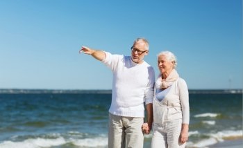 family, age, travel, tourism and people concept - happy senior couple walking and pointing finger on summer beach