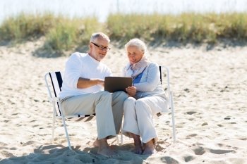 family, age, travel, tourism and people concept - happy senior couple with tablet pc computer sitting on deck chairs on summer beach