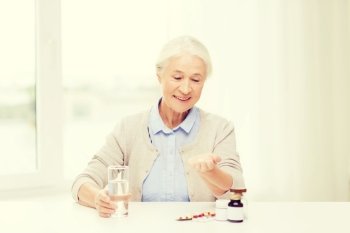 age, medicine, health care and people concept - happy senior woman with pills and glass of water at home