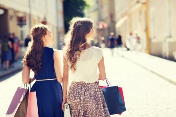 sale, consumerism and people concept - happy young women with shopping bags walking along city street