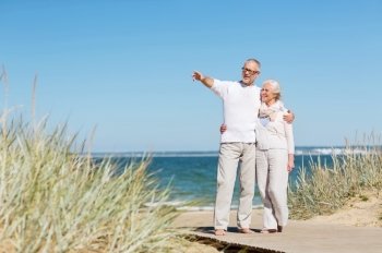 family, age, travel, tourism and people concept - happy senior couple hugging and pointing finger on summer beach