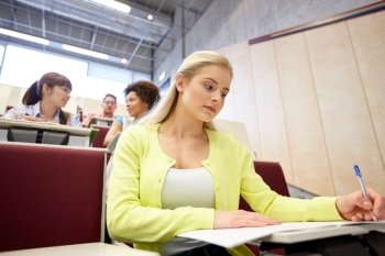 education, high school, university, learning and people concept - student girl writing to notebook at lecture hall