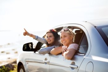 summer vacation, holidays, travel, road trip and people concept - happy teenage girls or young women sitting in car at seaside and pointing finger to something