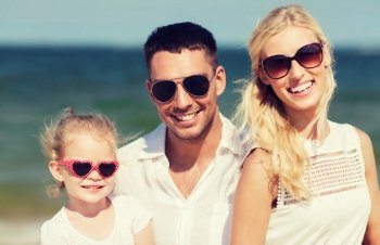 family,  vacation, adoption and people concept - happy man, woman and little girl in sunglasses on summer beach