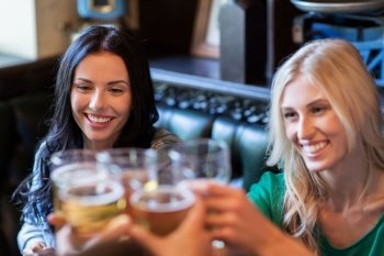 people, leisure, friendship and celebration concept - happy women drinking beer with friends and clinking glasses at bar or pub
