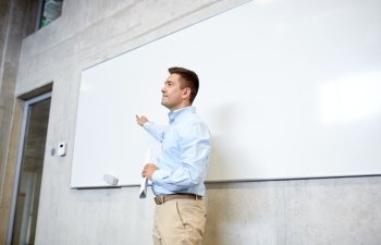 education, school, business, teaching and people concept - happy teacher or businessman pointing marker to white board at lecture