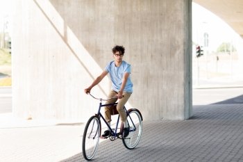people, style, leisure and lifestyle - young hipster man riding fixed gear bike on city street