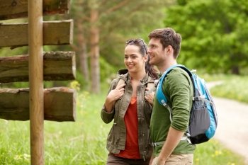 adventure, travel, tourism, hike and people concept - smiling couple with backpacks looking at signpost outdoors