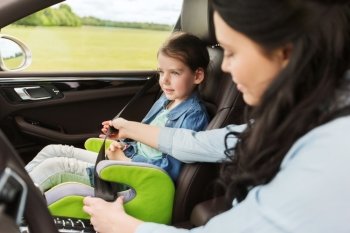 family, transport, road trip and people concept - happy woman fastening child with safety seat belt in car