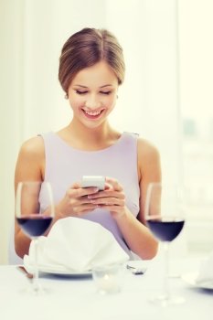 reastaurant, technology and happiness concept - smiling young woman with smartphone and glass of red wine at restaurant