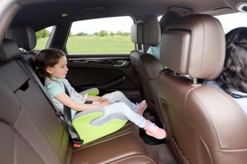 family, transport, road trip and people concept - happy little girl in safety seat driving in car