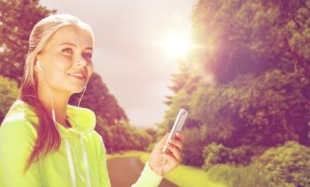fitness, sport, training, technology and exercising concept - sporty woman with smartphone and earphones listening to music outdoors over road and natural background