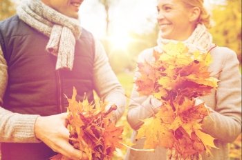 love, relationship, family, season and people concept - close up of happy smiling couple with pile of maple leaves having fun in autumn park