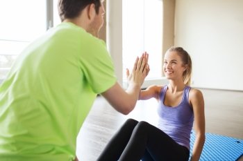 fitness, sport, training, teamwork and people concept - happy woman with personal trainer doing sit ups and high five gesture in gym