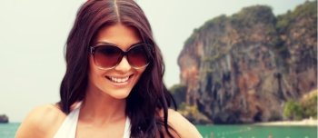 summer vacation, tourism, travel, holidays and people concept -face of smiling young woman with sunglasses over rock on bali beach background
