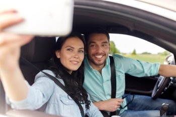 road trip, leisure, couple, technology and people concept - happy man and woman driving in car and taking selfie with smartphone