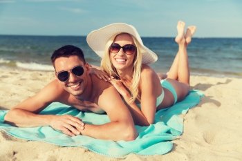 love, travel, tourism, summer and people concept - smiling couple on vacation in swimwear and sunglasses sunbathing on beach