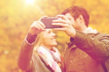technology, love, relationship and people concept - close up of smiling couple taking selfie with smartphone in autumn park