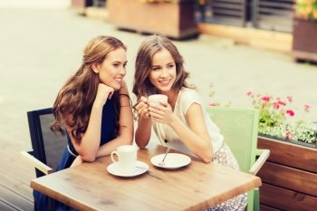 people, communication and friendship concept - smiling young women drinking coffee and talking at outdoor cafe