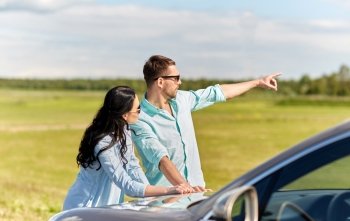 road trip, travel, tourism, family and people concept - happy man and woman searching location and pointing finger at car outdoors