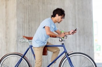 people, communication, technology and lifestyle - hipster man with smartphone, earphones and thermos cup on fixed gear bike listening to music on city street