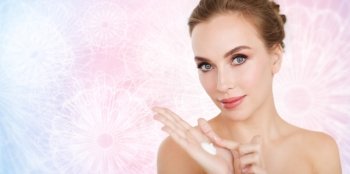 beauty, people, skincare and cosmetics concept - happy young woman with moisturizing cream on hand over rose quartz and serenity patterned background