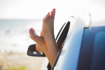 summer vacation, holidays, travel, road trip and people concept - close up of young woman feet showing from car window