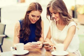 technology, lifestyle, friendship and people concept - happy young women or teenage girls with smartphones and coffee cups at cafe outdoors