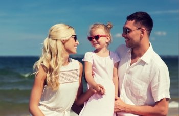family, vacation, adoption and people concept - happy man, woman and little girl in sunglasses on summer beach
