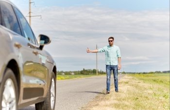 road trip, hitchhike, travel, gesture and people concept - man hitchhiking and stopping car with thumbs up gesture at countryside road