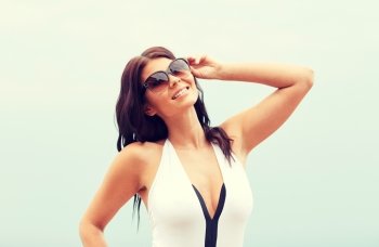 summer vacation, tourism, travel, holidays and people concept - smiling young woman in swimsuit with sunglasses on beach