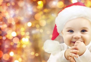 people, christmas, children and holidays concept - happy baby in santa hat over lights background